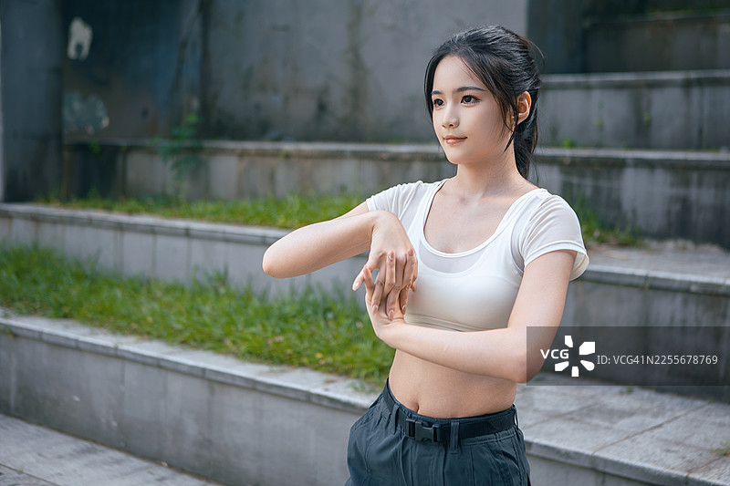 亚洲年轻女性在公园户外健身时伸展手臂，身穿运动背心，积极训练，健康的生活方式，锻炼习惯和养生理念。图片素材