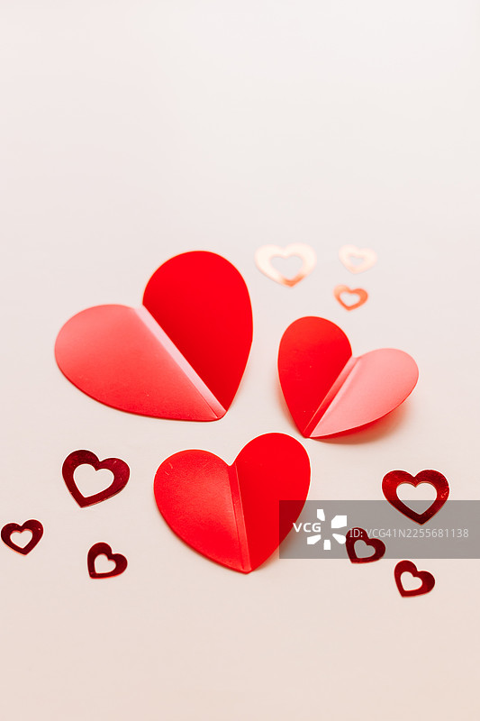 浅米色背景上排列的红色纸心。象征爱、情感和情人节庆祝的浪漫手工装饰。极简俯视构图，留有复制空间。图片素材
