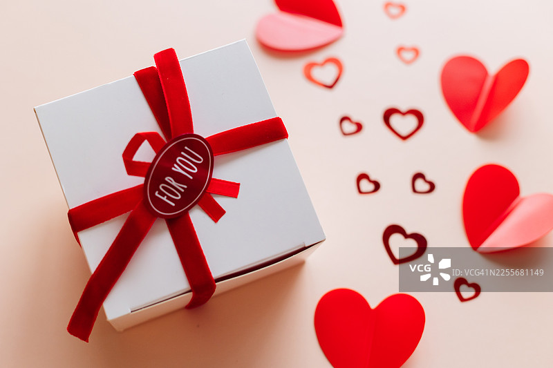 中性背景上装饰有心形图案的红丝带礼品盒。象征爱情、浪漫、惊喜和庆祝的 वैलेंट丁节礼物概念。俯视角度图片素材