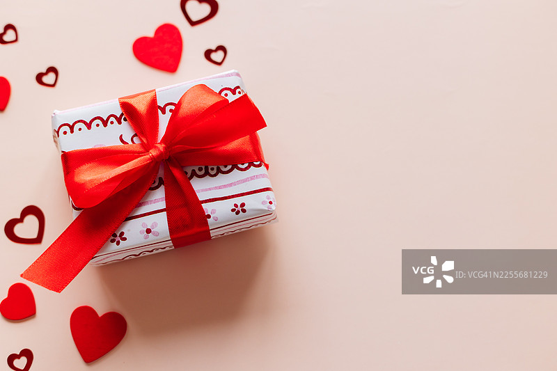 红丝带包装的礼品盒，中性背景上装饰着爱心。情人节礼物概念，象征着爱、浪漫、惊喜和庆祝。俯视角度图片素材