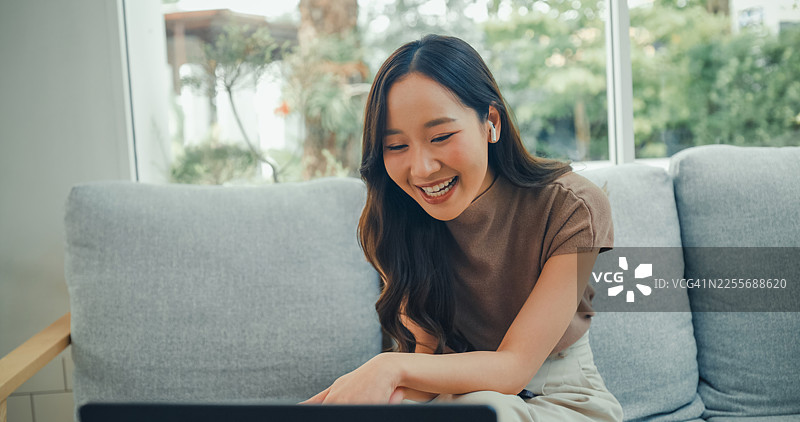 一位戴着耳机的年轻亚洲女性在舒适的咖啡馆里用笔记本电脑进行视频通话，她一边挥手一边享受咖啡。咖啡馆生活方式。图片素材