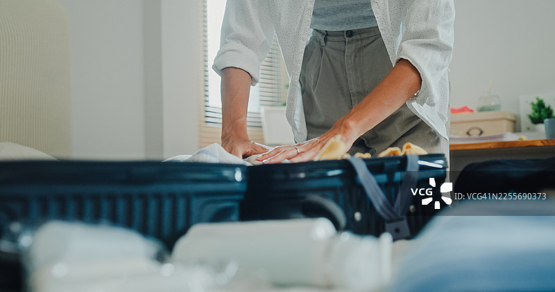 特写：年轻的亚洲女性在家里的卧室床上打包行李箱，为轻松的夏季度假旅行准备衣物和个人物品。图片素材