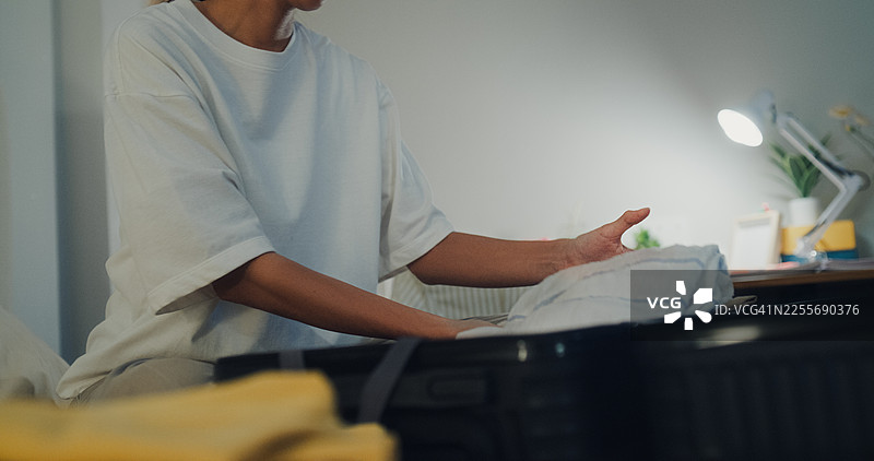 特写：一名年轻亚洲女子在家中卧室的床上，在准备衣物和个人物品，为夜晚放松的夏日假期旅行打包行李箱。图片素材