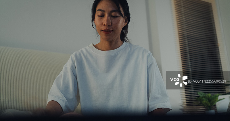 年轻的亚洲女性在家中的卧室里，在床上打包行李箱，为放松的夏季假期旅行准备衣物和个人物品，拍摄于夜晚。图片素材