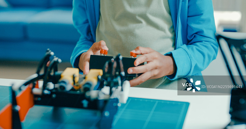 特写：一名年轻的非裔美国男孩在家中，在各种技术工具和模型中，使用遥控器进行机器人项目。STEM教育在线机器人课程。图片素材