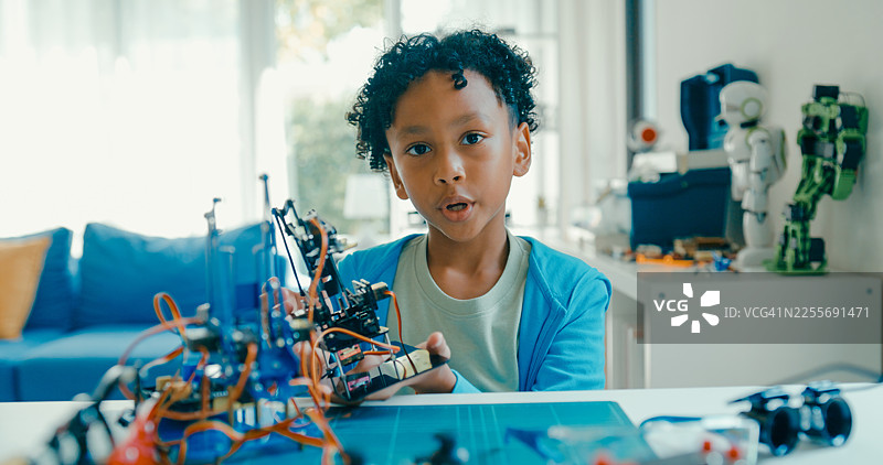 年轻的非裔美国男孩在家中解释他的机器人项目，展示了他的创作，并讨论了技术和创新。STEM教育在线机器人课程。图片素材