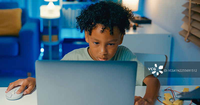 一名年轻的非洲裔美国男孩在家中夜晚学习编程代码，参与涉及机器人技术的STEM学习项目，在线STEM教育机器人课程。图片素材