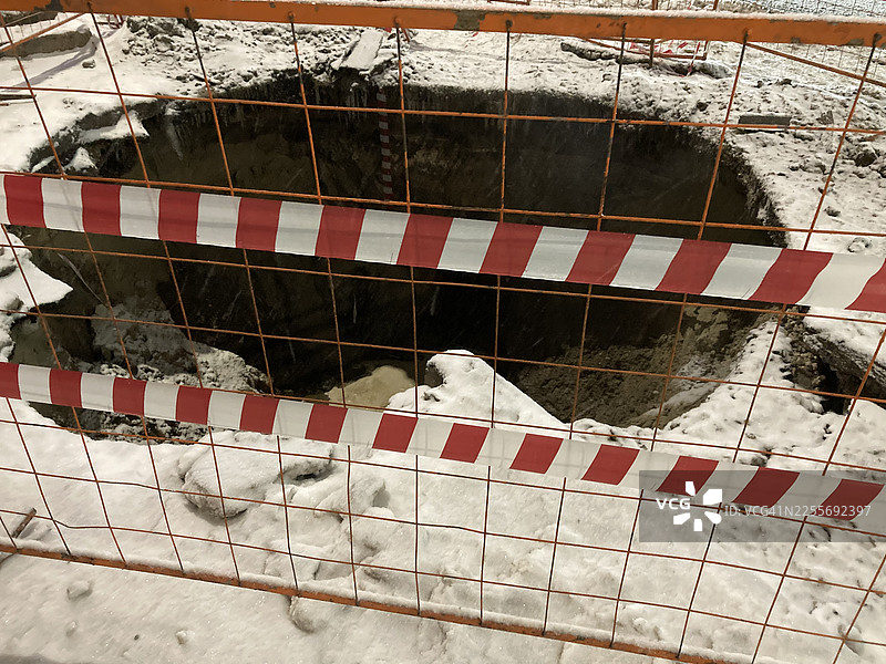 施工现场，雪地里的开放式建筑沟槽，有安全护栏和红白条纹胶带图片素材