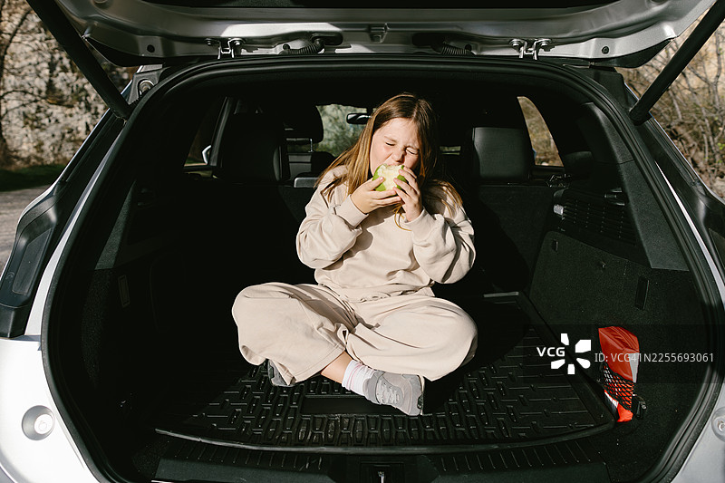 坐在一辆敞篷车的后备箱里，开心地吃着苹果的女孩图片素材