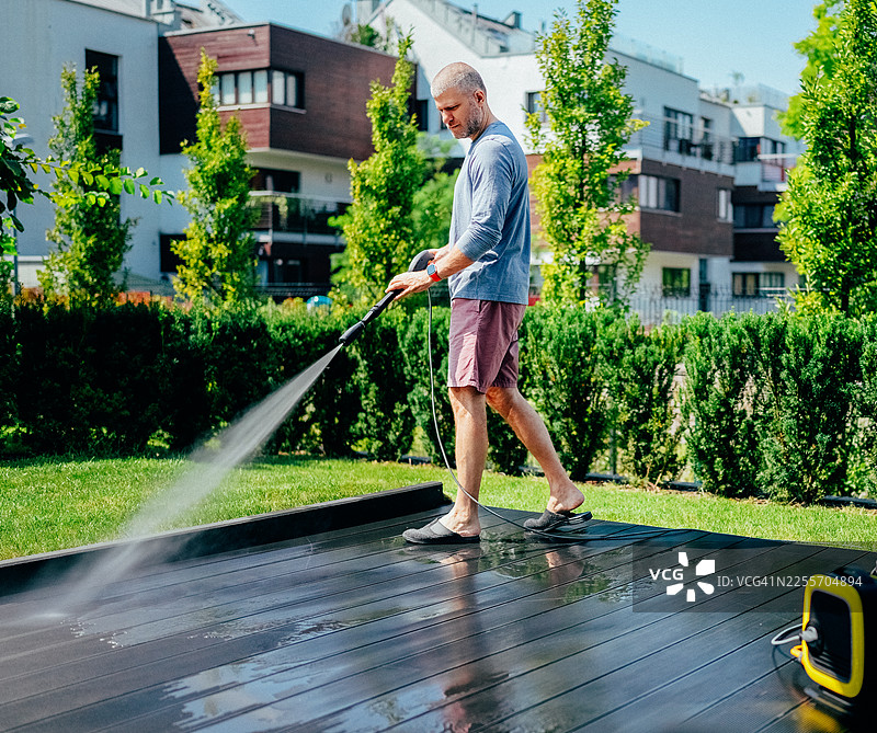 男人在现代后院花园里用高压清洗机清洗木制露台图片素材