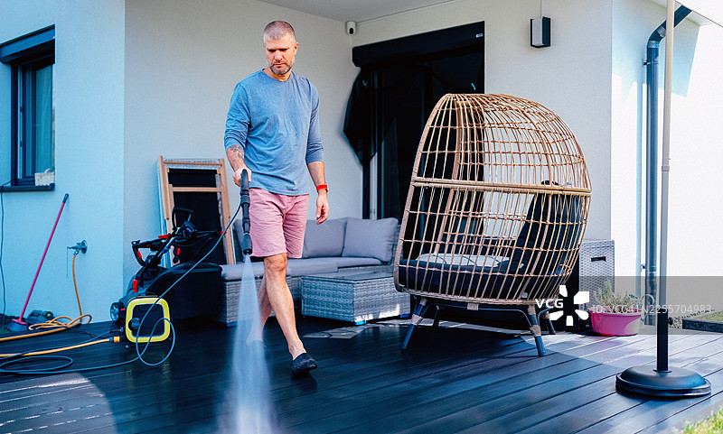 男士正在现代住宅的户外木质露台使用高压清洗机进行清洁图片素材