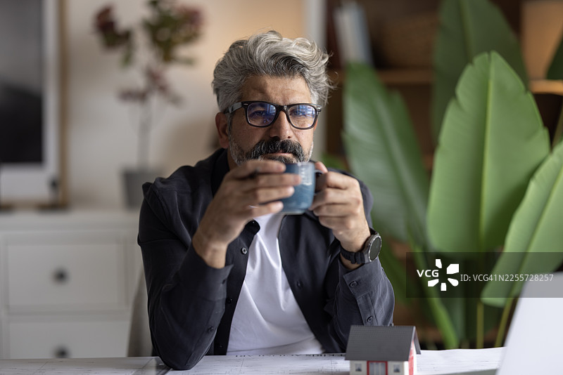 建筑师手持铅笔，在笔记本电脑和建筑蓝图前工作，工程师正在勾画建筑项目概念。图片素材