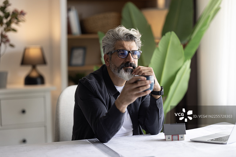 工程师手持铅笔，在笔记本电脑和蓝图上工作，绘制建筑规划图，构思建筑项目概念。图片素材