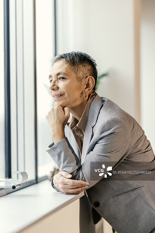 一位成熟的女商人，正在办公室的窗户边思考图片素材