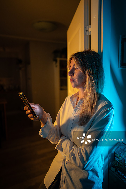 身处RGB灯光下的门廊，一位女士因情绪压力而沉思，并用智能手机浏览社交媒体。图片素材