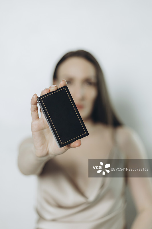 一位身穿浅色连衣裙的模糊女子在白色墙壁前展示一副黑牌。图片素材