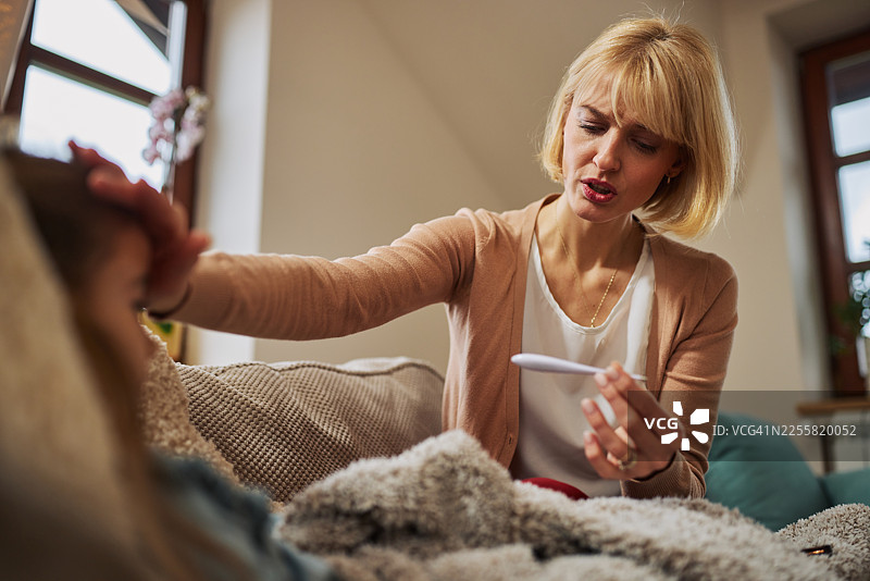 母亲在家照顾生病的女儿，用毯子和体温计安慰她图片素材