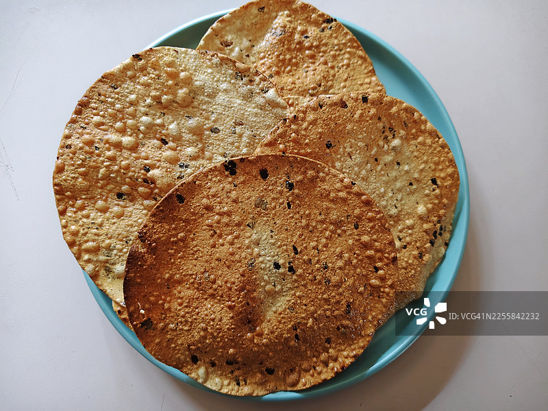 特写镜头，展示了油炸的马萨拉薄脆饼（papadams），这是一种受欢迎的、酥脆可口的印度小吃，盛放在陶瓷盘中/静物图片素材