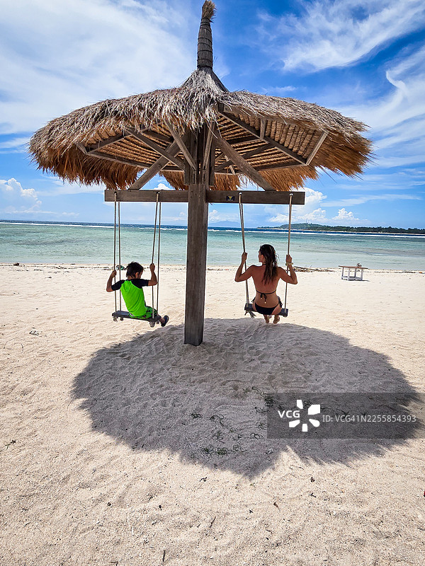 母亲和孩子在印度尼西亚吉利艾尔海滩的秋千上图片素材