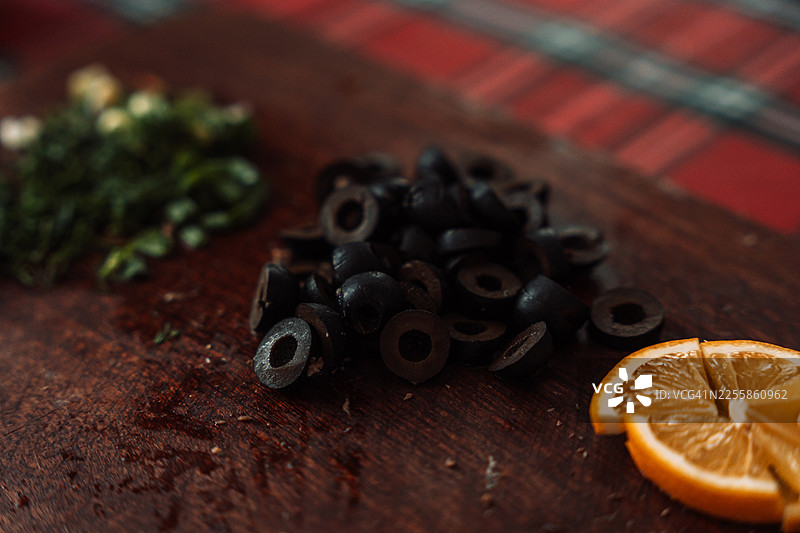 木质砧板上的黑橄榄片和切碎的香草，配以橙子片和格子背景图片素材