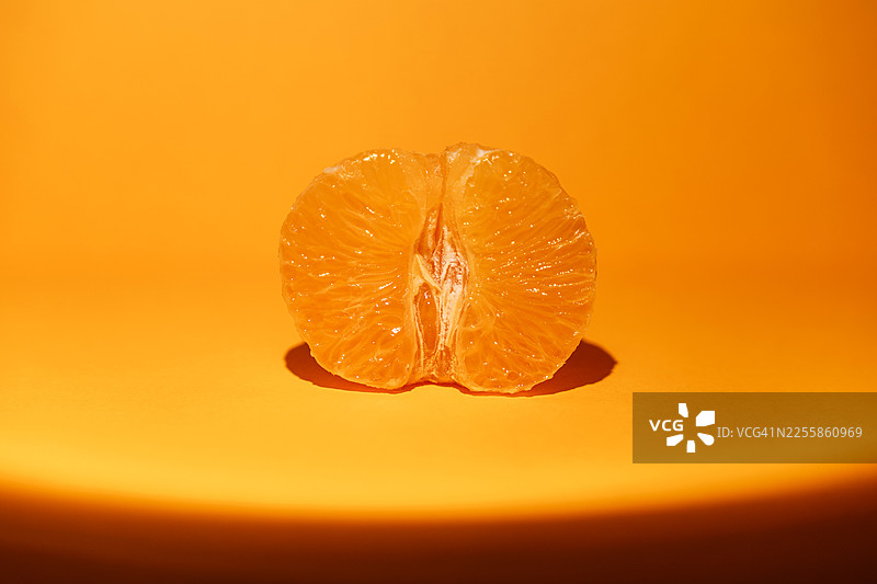 聚光灯下的半个橘子，背景为橙色图片素材