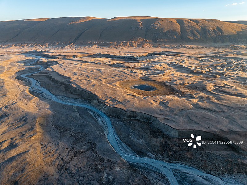 黎明时分，吉尔吉斯斯坦天山山脉高海拔高原上，一条宽阔蜿蜒的辫状冰川河切割着广袤大地，呈现出史诗般的空中全景。图片素材