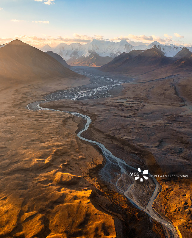 黎明时分，史诗般的垂直空中视角，展示了吉尔吉斯斯坦天山山脉红褐色高原上，一条宽阔、蜿蜒的辫状冰川河流切割而过。图片素材