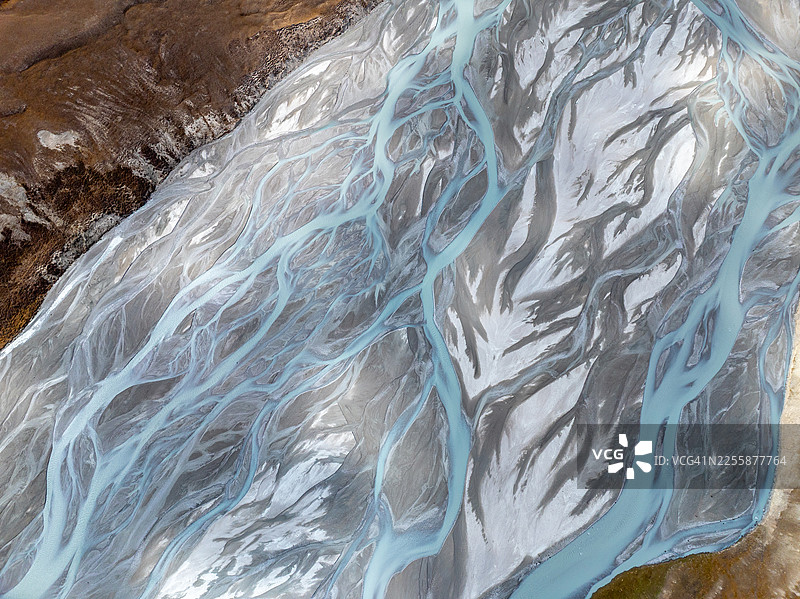 吉尔吉斯斯坦天山山脉高海拔高原上，一条广阔而复杂的辫状冰川河蜿蜒流淌，形成抽象的航拍图案，呈现出金棕色的色调。图片素材