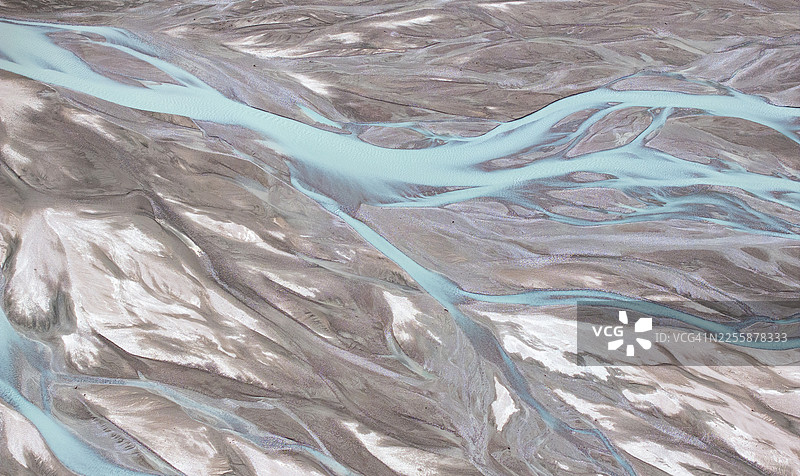 吉尔吉斯斯坦天山山脉高海拔金色高原上，蜿蜒交错的冰川河流呈现出抽象的空中视角图案。图片素材