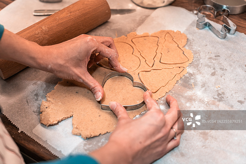 在烘焙纸上用饼干模具切割心形姜饼干，为圣诞节在家烘焙做准备，俯视角度图片素材