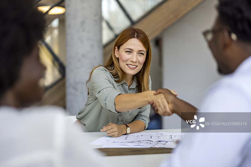 在现代办公室的商务会议中，一位职业女性与同事握手图片素材