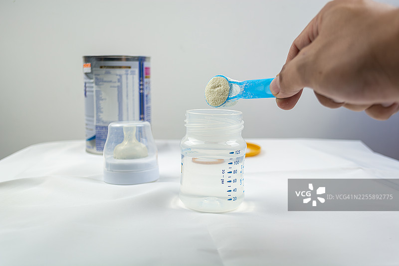 浅色背景下特写奶粉和蓝色勺子。罐子里的婴儿配方奶粉用量勺。婴儿奶粉和勺子。婴儿奶粉和奶瓶图片素材