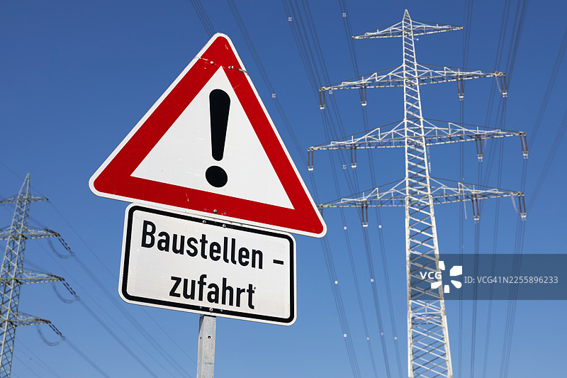 建筑工地上的警告标志，背景是高耸的电力塔图片素材