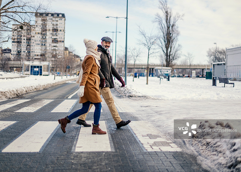 一对年长的夫妇微笑着走过雪中的城市人行横道图片素材