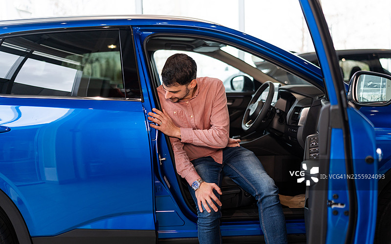 年轻男子在展厅试驾一辆新的蓝色汽车图片素材