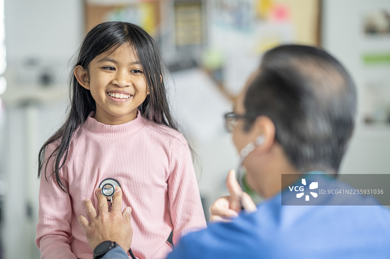 微笑的年轻亚洲女孩在明亮的儿科诊所看医生图片素材