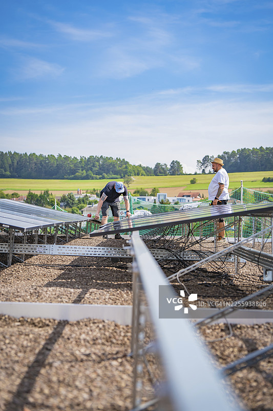 两名男子在乡村田野环绕的建筑工地上安装太阳能电池板,这是位于德国卡尔夫赫尔曼·黑塞铁路上的新卡尔夫·霍伊马登停车场(Park and Ride Calw Heumaden)。图片素材