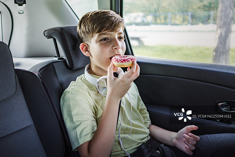 小男孩坐在汽车后座，在漫长的假期旅途中享用甜甜圈。图片素材