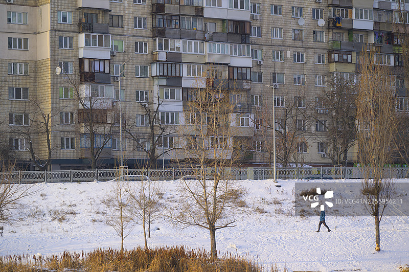 一个人在雪地里的城市景观中，背景是居民楼图片素材