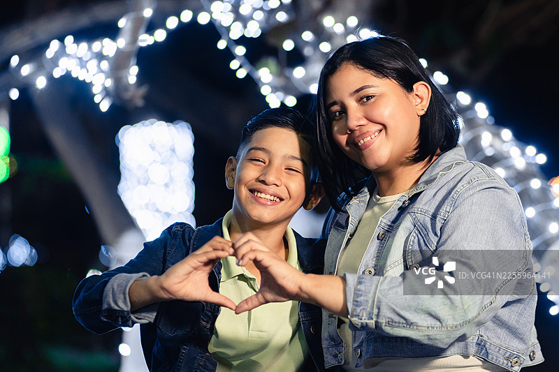 夜市里，一位拉丁裔女子和孩子正在做出爱心手势图片素材