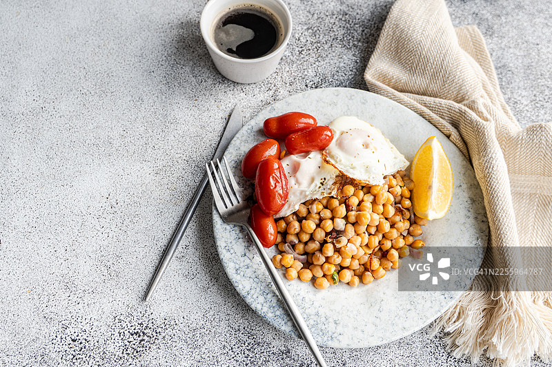鹰嘴豆沙拉的俯视视图，配有红洋葱、石榴、香菜、煎蛋、西红柿和一杯黑咖啡图片素材