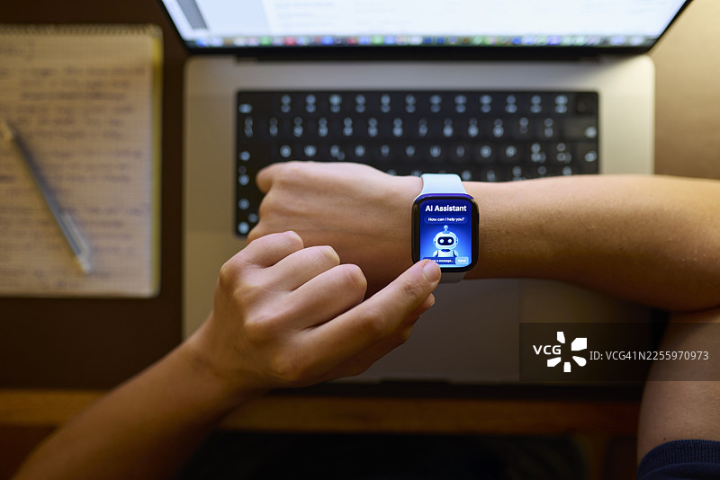 俯视角度，一名男子在书桌前使用智能手表上的AI助手图片素材