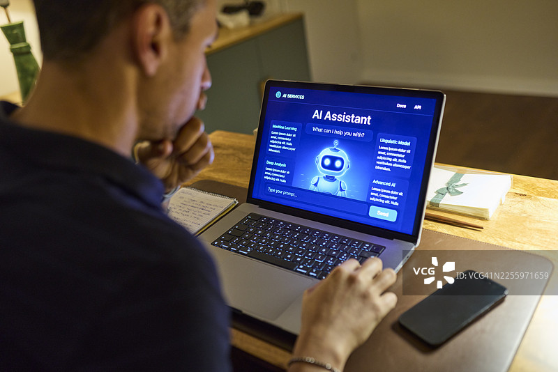 夜间在家中，一名男子在书桌前使用笔记本电脑上的AI助手图片素材