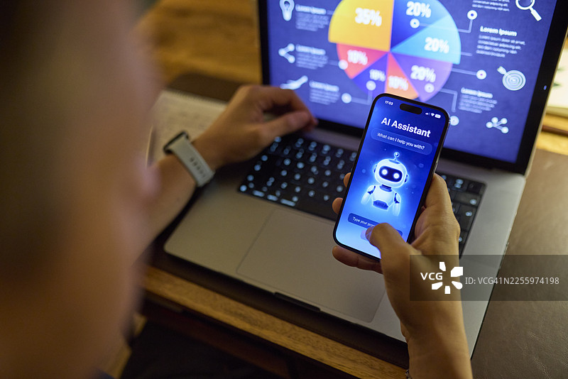 晚上，一名男子在家里的书桌上，通过笔记本电脑和智能手机与人工智能助手一起分析数据图片素材