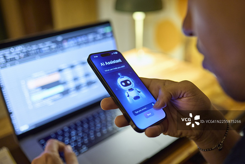 晚上在家，男子在笔记本电脑前使用智能手机上的AI助手图片素材