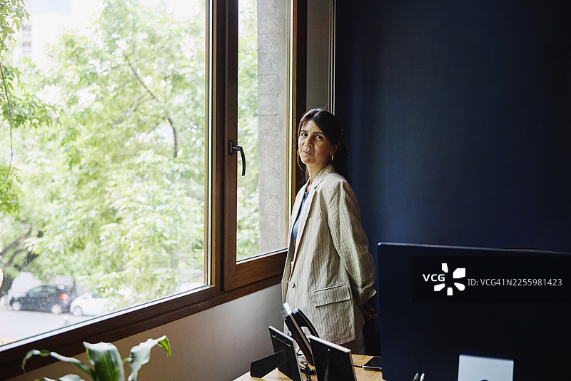 中景办公室窗前站立的女商人的肖像图片素材