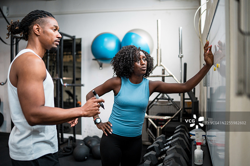中年黑人女性与健身教练在现代健身房讨论健身目标图片素材