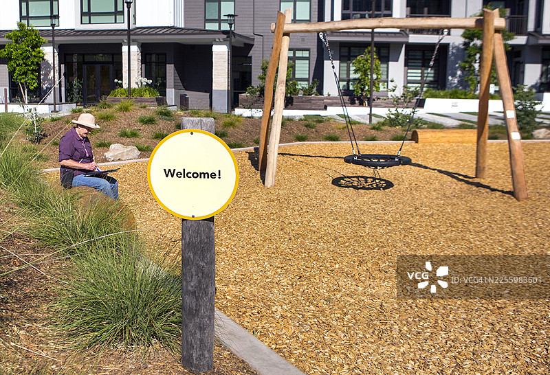 一位戴着草帽的老年人在公园里独自坐着，在平板电脑上写字图片素材