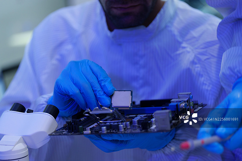 国际男女技术人员穿着无菌服在半导体制造厂使用显微镜工作（照片）图片素材