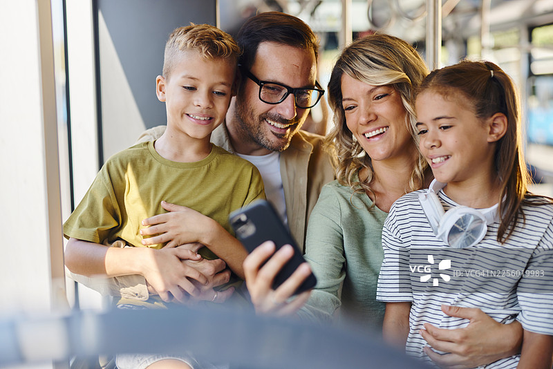 快乐的一家人乘坐公共交通工具旅行，同时使用手机。图片素材